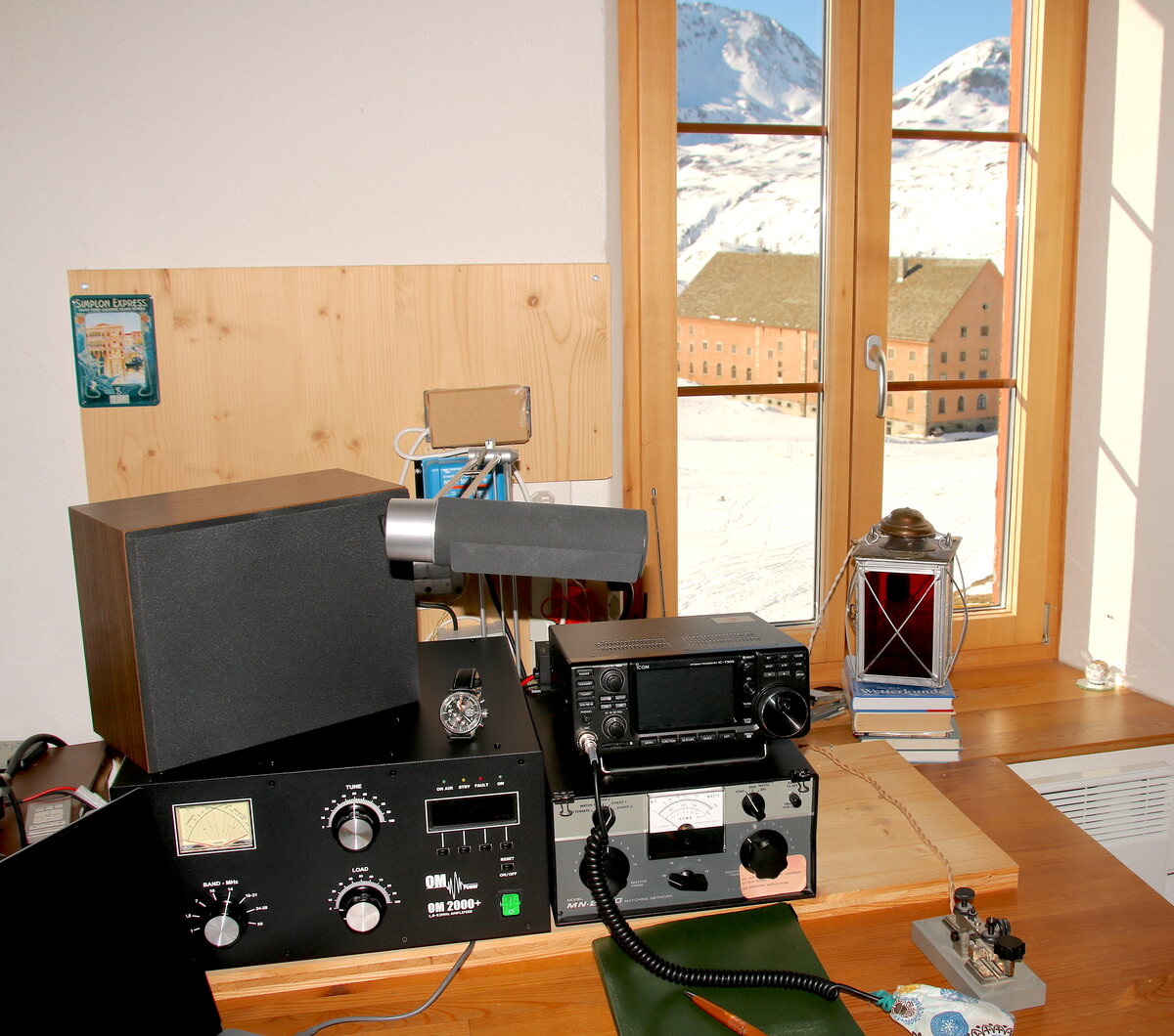 Funkstation mit Kurzwellen-Transceiver, Endstufe und Morsetaste vor einem Fenster mit Blick auf verschneite Berge