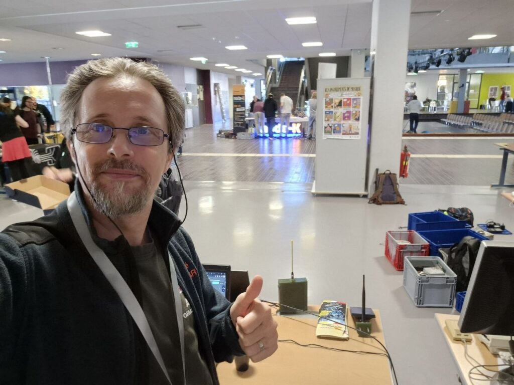 André OE8ASR macht ein Daumen-hoch-Selfie am Stand von KÄRNTEN FUNKT in der Halle des IT-Gymnasiums
