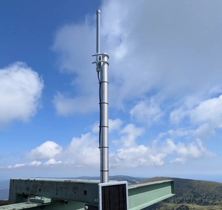 Der Repeater AT-WO-Koralpe: Antenne auf dem Mast, darunter ein Solarpanel, dahinter die Berge der Koralpe