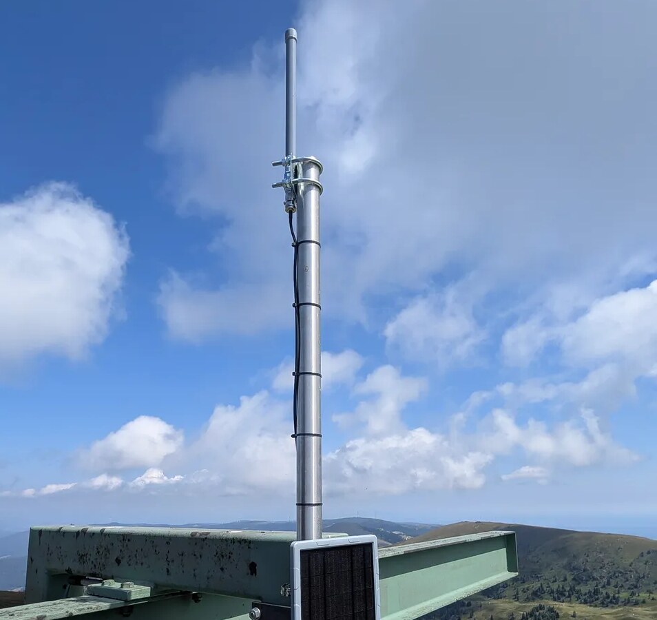 Der Repeater AT-WO-Koralpe: Antenne auf dem Mast, darunter ein Solarpanel, dahinter die Berge der Koralpe